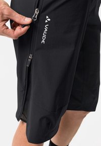 Schwarze Shorts aus leichtem Material, ausgestattet mit einer Reißverschlusstasche, glatter Textur und einem Logo an der Seite.