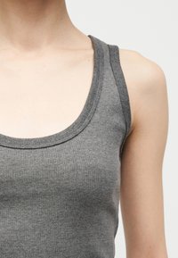 Κοντινό πλάνο ενός ατόμου που φοράει αμάνικο γκρι ριμπ μπλουζάκι, δείχνοντας τον λαιμό, τον ώμο και την πάνω περιοχή του στήθους.