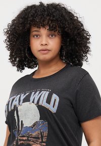 Černé tričko s krátkým rukávem s grafickým designem a textem "STAY WILD" a scénou pouště, vyrobené z měkké tkaniny s volným střihem.