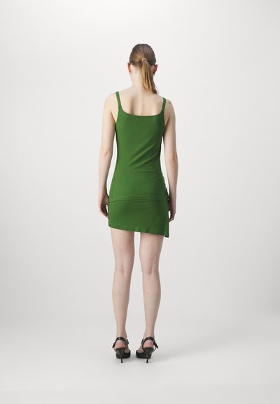 Robe verte ajustée à bretelles spaghetti, longueur genou, texture lisse, associée à des sandales à talons hauts noires.