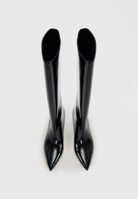 Stivali neri in pelle fino al ginocchio con finitura lucida, punta affusolata e gambale strutturato; senza hardware o decorazioni visibili.