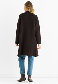 Brown wool blend long coat with a collar, oversized sleeves, and a straight silhouette, paired with blue jeans and patterned ankle boots.