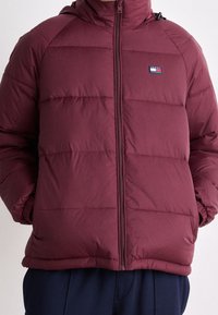 Giacca imbottita bordeaux con zip frontale, design trapuntato e patch con logo sul lato sinistro del petto. Presenta un cappuccio e polsini elasticizzati.