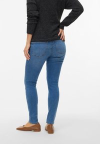 Μπλε στενά τζιν με μεσαία μέση, χαρακτηριστική σχεδίαση με πέντε τσέπες, και ομαλή υφή τζιν. Φορώντας τα με σκούρο πουλόβερ και καφέ μπαλαρίνες.