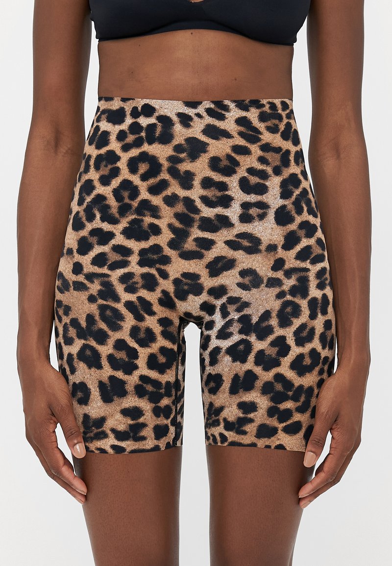 Woman wearing high-waisted, leopard print biker shorts and a black sports bra, standing with arms relaxed by her sides.