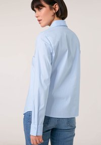 Light blue striped shirt with a collared neckline, long sleeves, and buttoned cuffs. Material appears smooth with a structured fit.