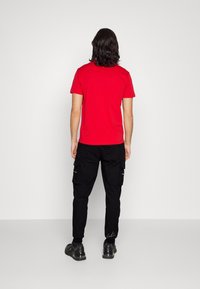 Röd kortärmad t-shirt, svarta cargosbyxor med sidofickor och svarta skor. Byxorna har en distinkt elastisk mudddesign.