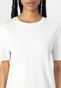 Vit kortärmad t-shirt med rund halsringning, slät textur och avslappnad passform. Har en minimalistisk design utan synliga logotyper eller mönster.