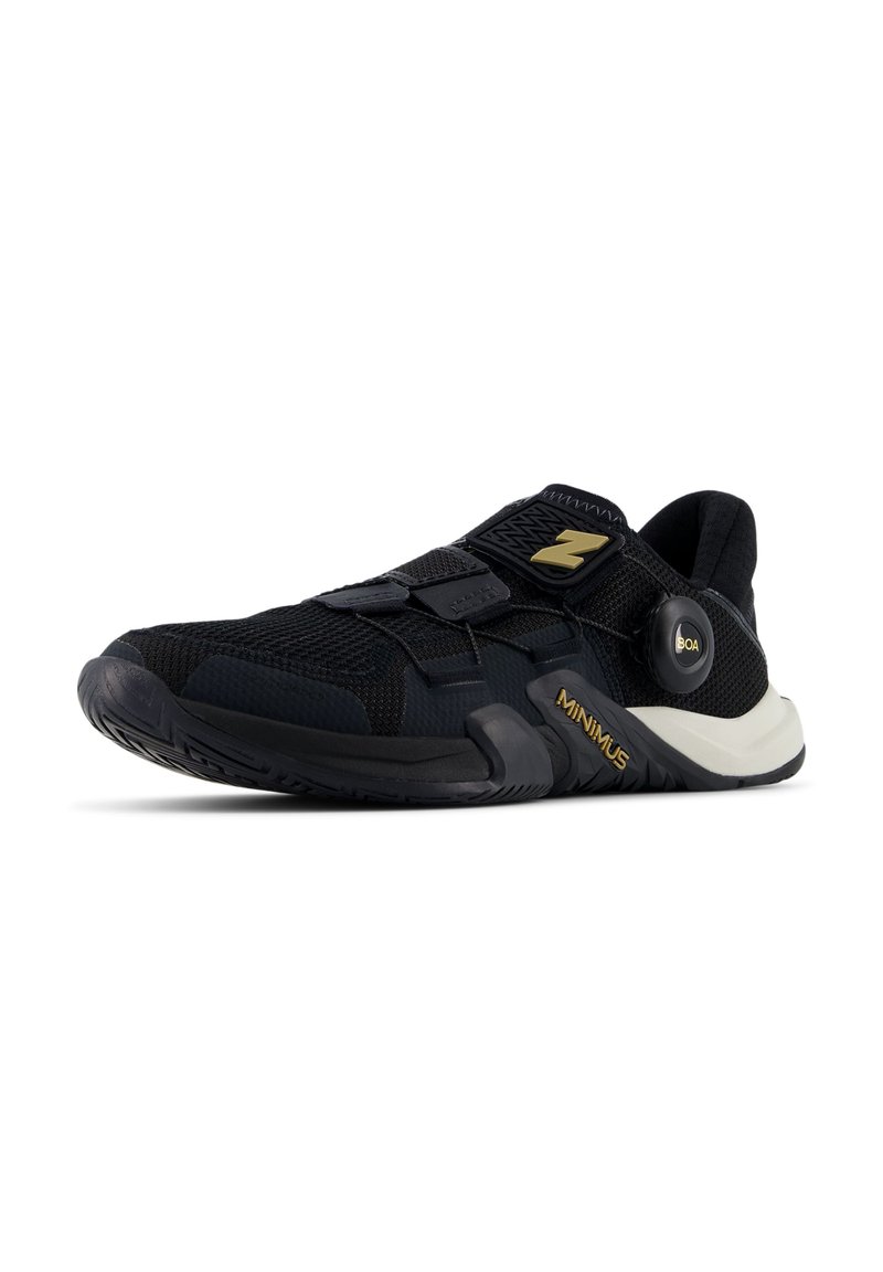 Zapatilla deportiva negra con parte superior de malla, tiras de Velcro y sistema de cordones BOA. Cuenta con una suela texturizada y acentos dorados en el costado.
