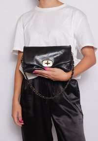 Borsetta nera in pelle con finitura lucida, chiusura a scatto in tono oro e tracolla a catena. Il design è rettangolare con bordi morbidi.