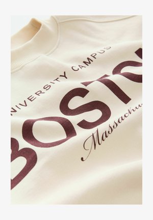 Krém színű pulóver, nagy bordó szöveggel: "Boston" és "University Campus, Massachusetts." Bordás nyakkivágás és puha textúra.