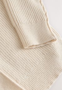 Vêtement tricoté de couleur crème avec une texture côtelée. Le tissu a un aspect doux et duveteux et est orné d'un large bord-côte à la manche.