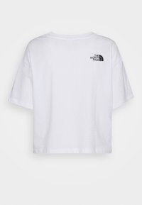 Bílý, zkrácený tričko vyrobené z bavlny s kulatým výstřihem. Vyznačuje se černým logem na horní části zad. Krátké, volně padnoucí rukávy.