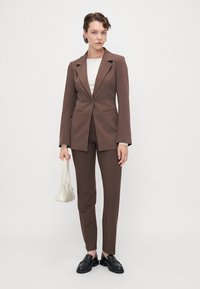 Brun tilpasset dress med en blazer med en enkelt knapp, slim-fit bukser og en ensfarget hvit topp. Tilbehøret inkluderer en liten veske.