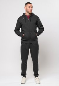 Fekete, kapucnis, cipzáros kapucnis dzseki, elülső zsebekkel és szürke részletekkel, fekete, puha, textúrált anyagú joggerváltozattal párosítva.