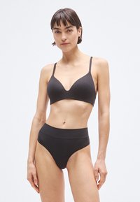 Soutien-gorge sans fil noir avec un décolleté plongeant et des bretelles réglables, associé à une culotte noire taille haute et sans coutures. Texture lisse.