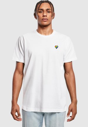 Witte katoenen t-shirt met een klein regenboog hartlogo op de linkerborst. Klassieke ronde hals en korte mouwen met een loose fit.