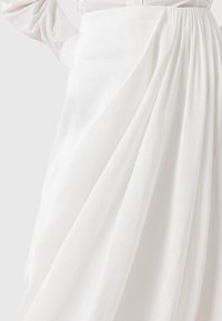 Biała spódnica z materiału o miękkich, zwiewnych fałdach; lekką teksturą; posiada detal w postaci ściągniętej talii; gładkie wykończenie podkreśla prostotę.