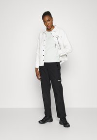 Casaco acolchoado branco sobre uma blusa verde-clara, combinado com calças pretas e sapatos pretos. Inclui um bolso frontal no casaco.
