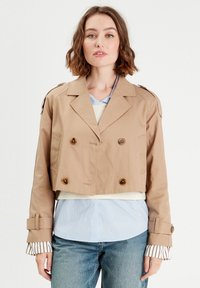 Veste beige cropped à double boutonnage avec des boutons marron, épaulettes et manchons rayés contrastants sur une chemise bleu clair.