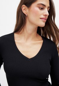 Black ribbed long-sleeve top with a V-neckline. Features a fitted design and smooth texture. Subtle stitching details enhance the appearance.