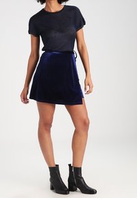 Camiseta nera a maniche corte abbinata a una minigonna in velluto blu. L'outfit è completato da stivaletti neri alla caviglia con dettagli in cerniera.