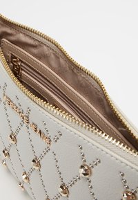 Pochette en similicuir texturé blanc avec quincaillerie dorée, ornée de strass et dotée d'une poche zippée à l'intérieur.