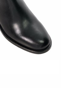 Bottine noire en cuir avec une texture lisse, un bout pointu et un moindre détail de couture le long de la semelle. Construction légère.