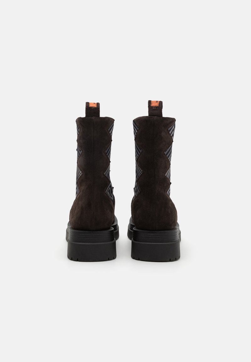 Stivali ankle in suede marrone scuro con tessuti a zigzag sui lati, una suola nera spessa e linguette per un facile indossamento.