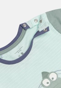 Camiseta corta de bebé de color verde menta claro con rayas verticales blancas, cuello redondo azul marino y un gráfico de una rana de dibujos animados en el frente.