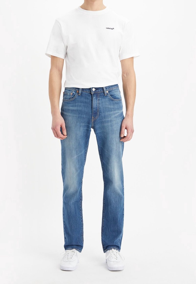 White cotton t-shirt with "Levi's" logo, paired with blue denim jeans featuring a straight cut, light distressing, and classic 5-pocket design.