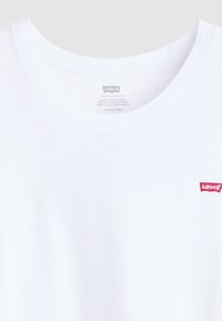 Camiseta de algodón blanca con cuello redondo, que presenta un pequeño logo rojo de Levi's en la parte izquierda del pecho. Textura suave, diseño simple.