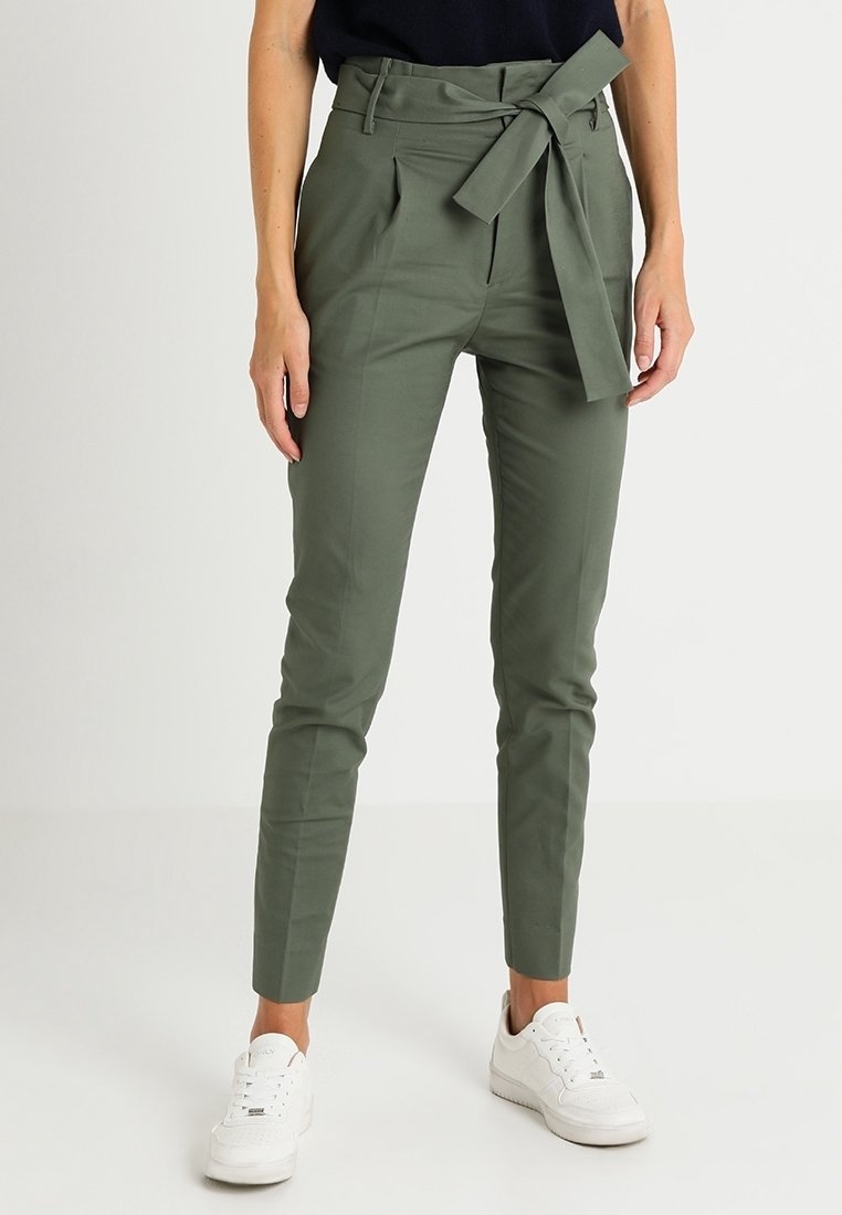 Olivgrön högmidjad byxor med bälte i midjan, framfällt och avsmalnande ben, i kombination med vita sneakers.
