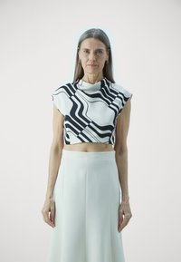 Black and white cropped top with abstract wavy lines, featuring a draped collar. Paired with a high-waisted white skirt with pleats.