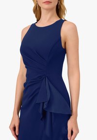 Marineblaue Kleid mit ärmellosem Design, das einen gerafften Oberteil und ein asymmetrisches Volantdetail auf der linken Seite für zusätzlichen Textur beinhaltet.