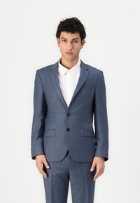 Blauer Karo-Anzug mit einem Zwei-Knopf-Verschluss, Reverskragen und zwei vorderen Taschen. Getragen über einem weißen Hemd.