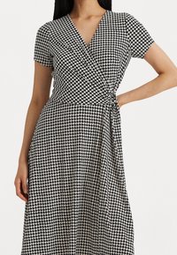 Sukienka w czarno-białą kratę houndstooth, z krótkimi rękawami, dekoltem w serek, wiązanym w pasie i zwiewnym materiałem.