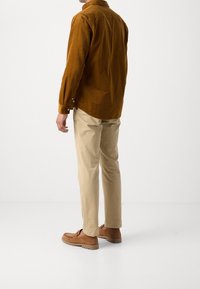 Camisa de pana marrón, pantalones chinos beige y mocasines marrones. La camisa presenta un cuello con botones y mangas largas con puños. Diseño limpio y minimalista.