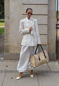 Baltas pritaikytas švarkas, baltos plačios kelnės, kūno spalvos rankinė su juodais akcentais ir nuogos smailianosiai. Lygaus audinio, minimalistinio dizaino.