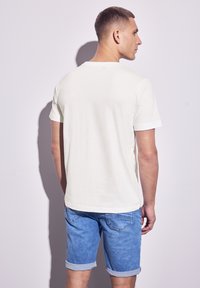 Bílý bavlněný tričko s krátkým rukávem, volný střih a kulatým výstřihem. Nosené s světle modrými denimovými šortkami, které mají ohrnuté manžety a kapsy.