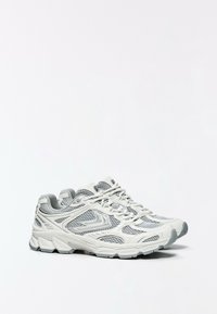 Paire de chaussures de course athlétiques blanches et grises avec des panneaux en mesh et des lacets sur un fond blanc uni.