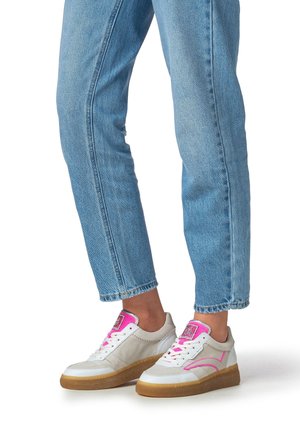 White sneakers with pink accents, a textured fabric upper, and a gum rubber sole, paired with light blue denim jeans.