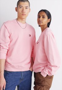 Sudaderas rosas con puños y cinturillas acanaladas, que presentan pequeños acentos de logotipo. El material parece suave con un diseño de ajuste relajado.
