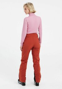 Maglia rosa a maniche lunghe abbinata a pantaloni da sci rossi. I pantaloni presentano gambe dritte con dettagli neri, progettati per gli sport invernali.