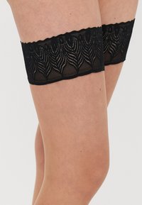 Meias pretas até à coxa de renda com topo ondulado com padrão de ondas, tecido semitransparente e ajuste justo para uso seguro.