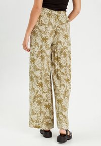 Szerokie spodnie z kwiatowym i liściastym wzorem w oliwkowym i kremowym kolorze. Elastyczny pas, lekki materiał i boho design.