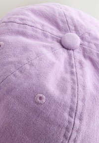 Lila texturerad keps med en rund toppknapp, sömnadssämmar och små broderade detaljer i en liknande nyans.