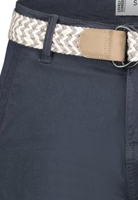 Navy blue pants with a woven grey and white braided belt, featuring a tan leather buckle and strap, highlighting textured materials and stitching.