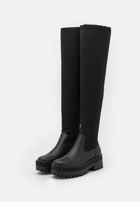 Botas negras hasta la rodilla con parte superior de punto y suela de plataforma de goma con detalles estriados. Sección del pie de cuero suave y lados elásticos.