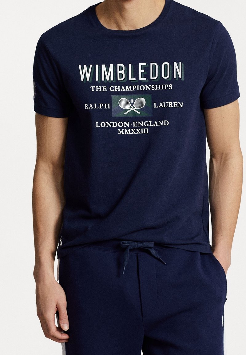 Námořnická modrá bavlněná tričko s nápisem "Wimbledon", grafikou tenisové rakety a uvolněným střihem. Krátké rukávy a kulatý výstřih.